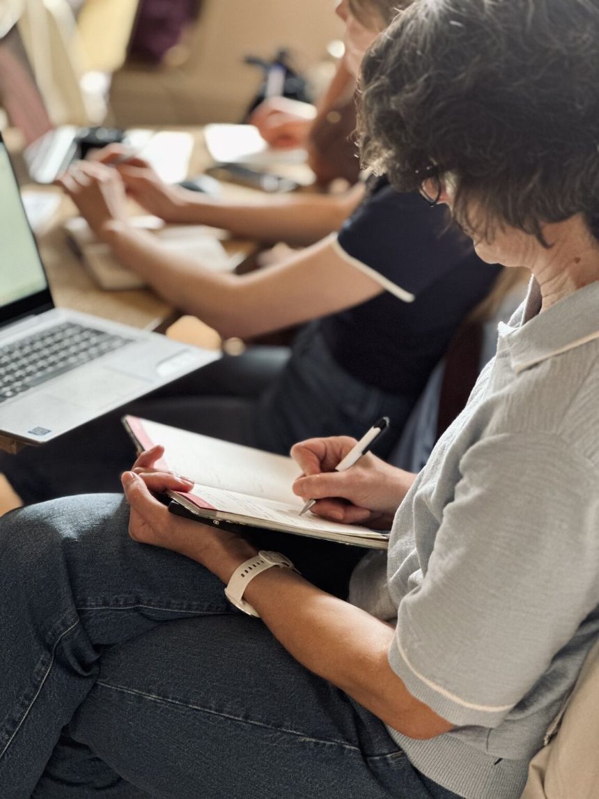 A member writing notes by hand next to her laptop at a Zorya AI meetup